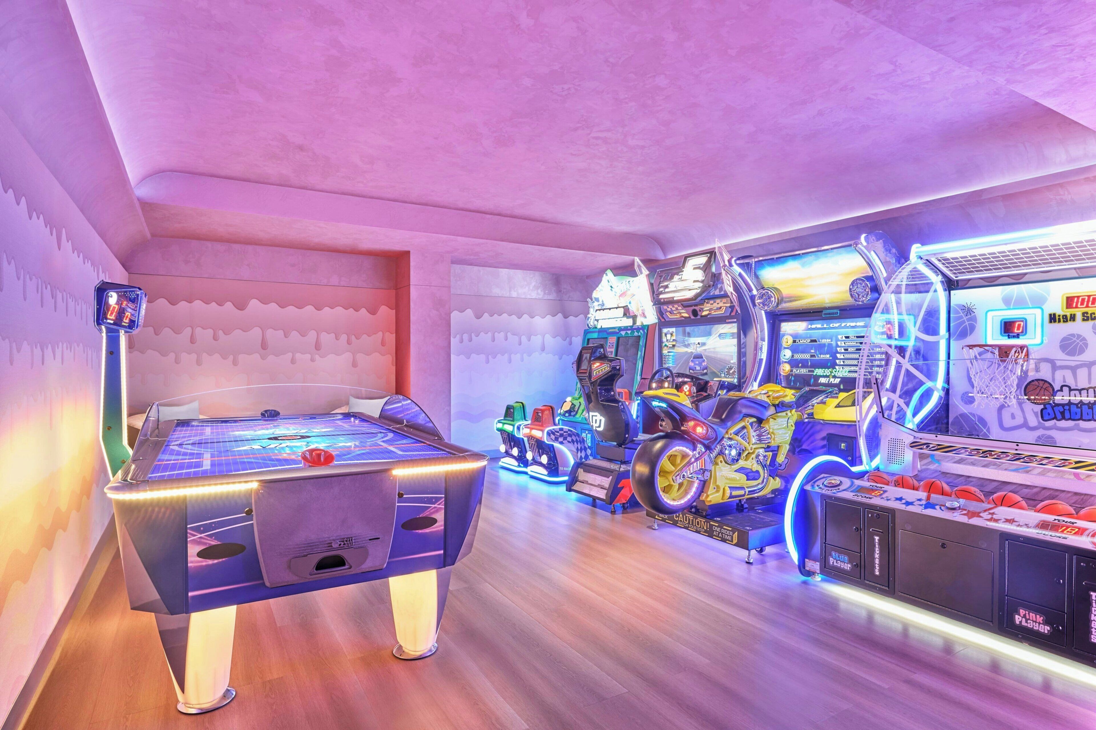 A room with a pool table, arcade games, and a basketball shooting game.