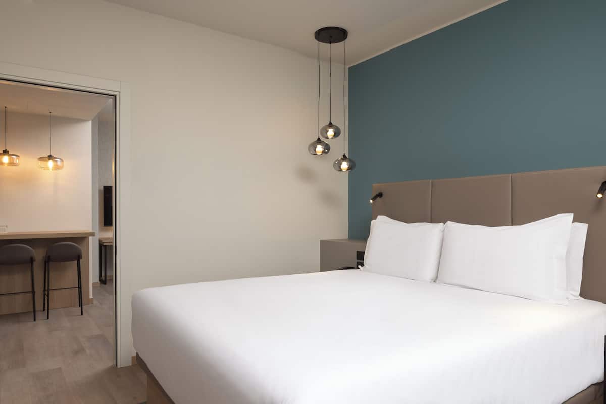 A modern hotel room with a large bed, a desk with two chairs, and pendant lighting.