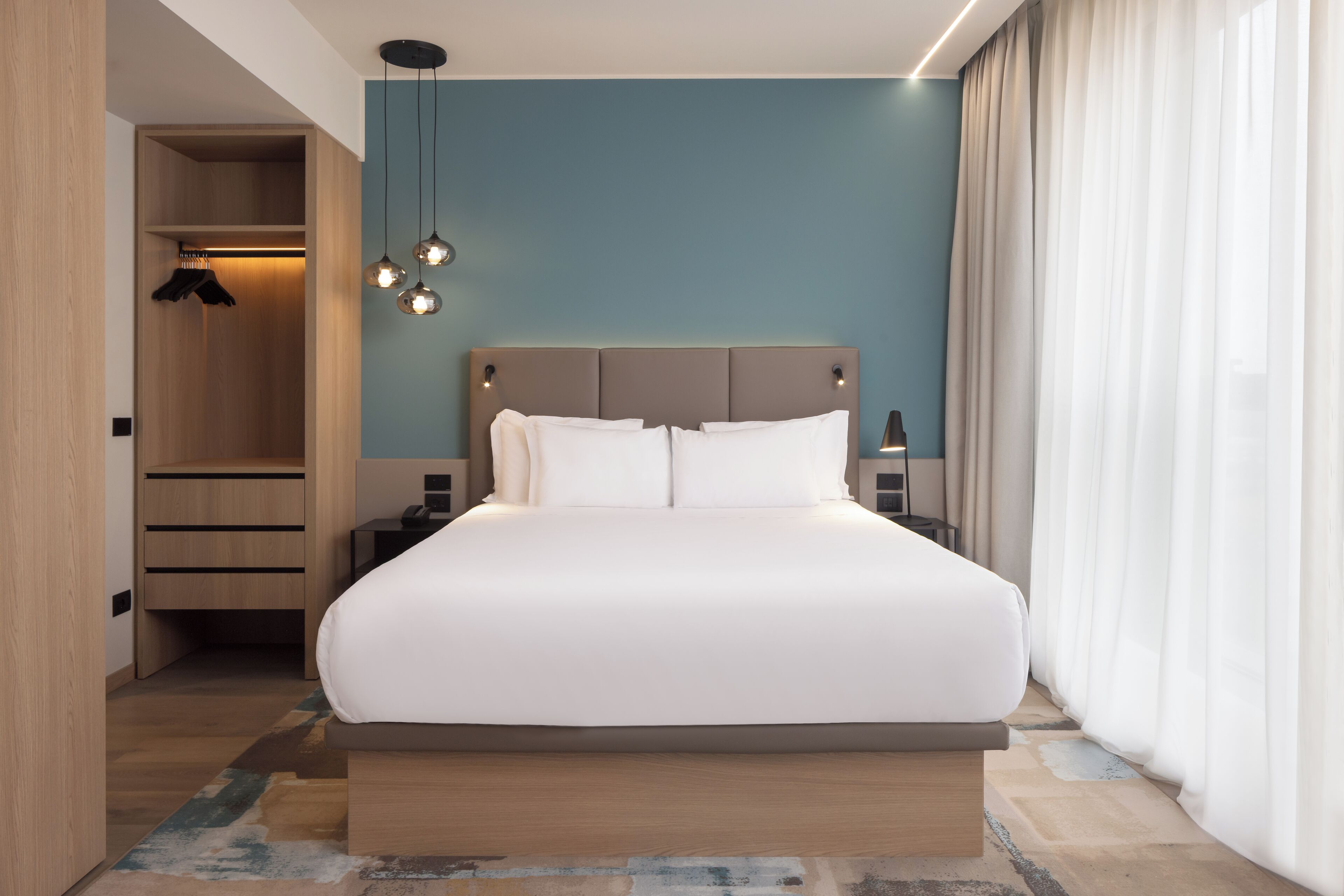 Ein modernes Hotelzimmer mit einem großen Bett, einem Holzschrank und einem Nachttisch mit Lampe.