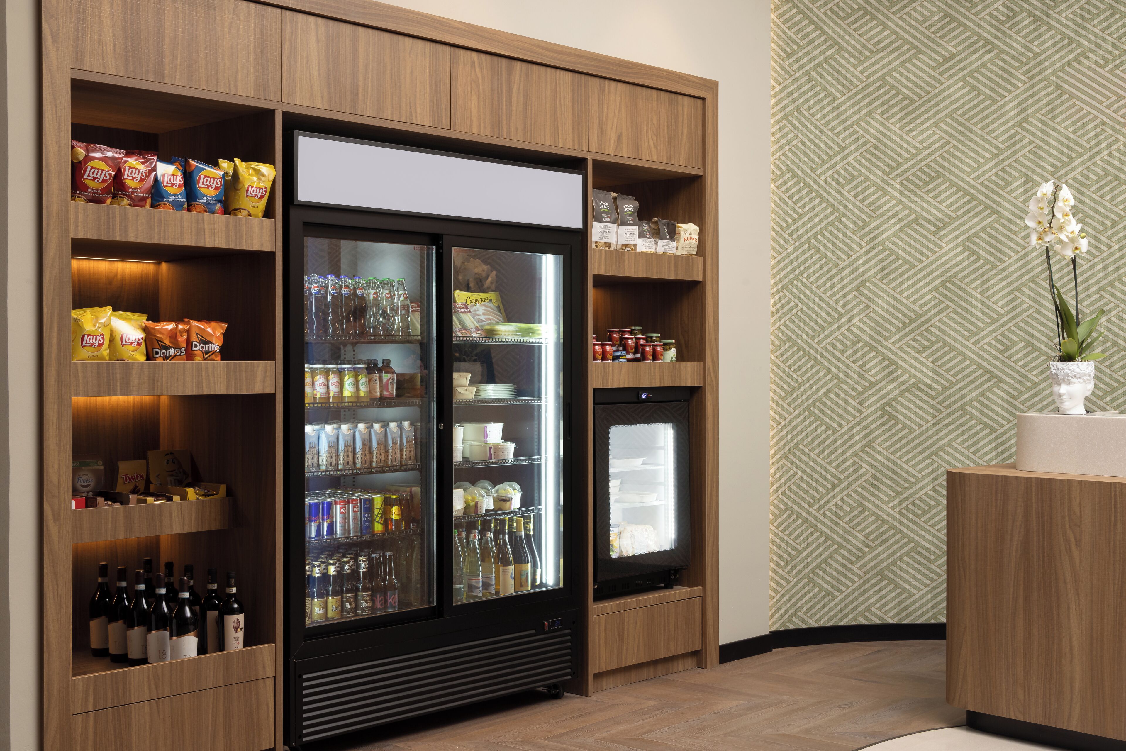 A hotel room with a minibar stocked with snacks, beverages, and condiments.