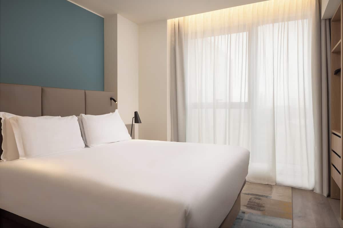 A neatly made bed with white linens, a headboard, and a bedside table with a lamp.