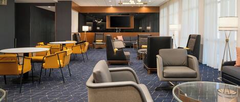 A hotel lobby with a seating area, a flat-screen TV, and a coffee bar.