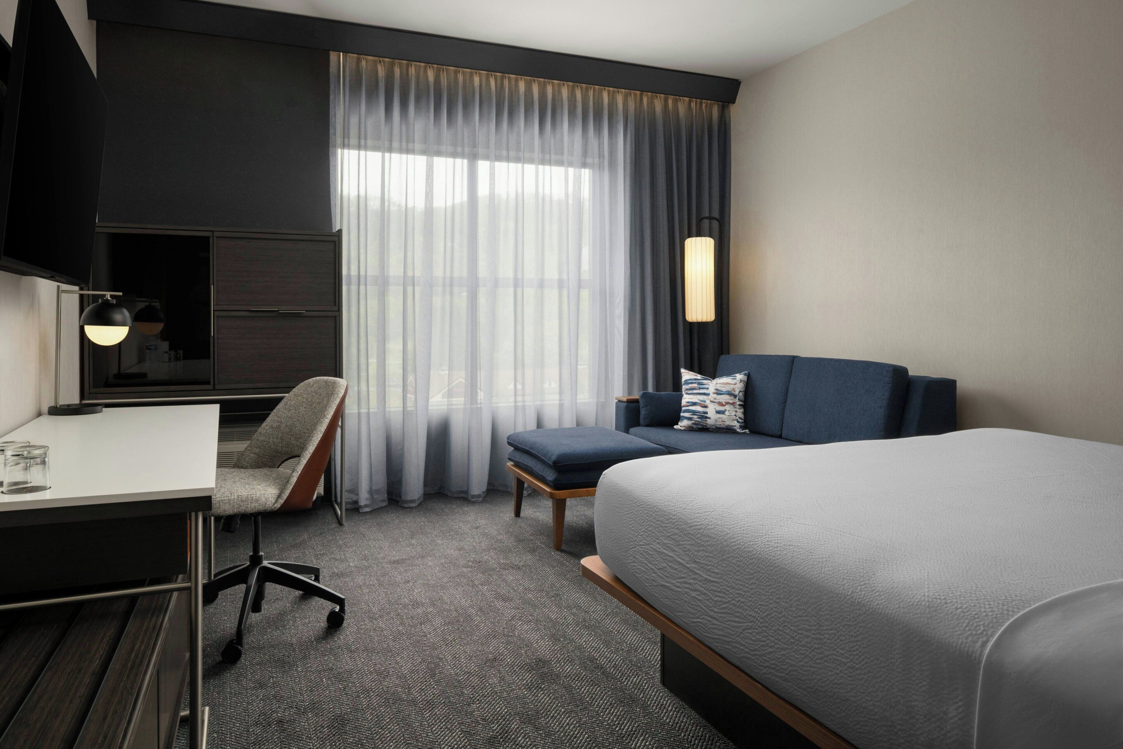 Een hotelkamer met een bed, een bureau, een stoel, een televisie en een raam met gordijnen.