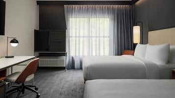 Una habitación de hotel con cama, escritorio, silla y un ventanal con cortinas.