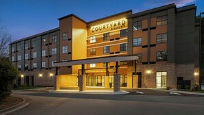 Un hotel de varios pisos con un llamativo letrero de 'Courtyard by Marriott', un acceso cubierto y fachada de ladrillo.