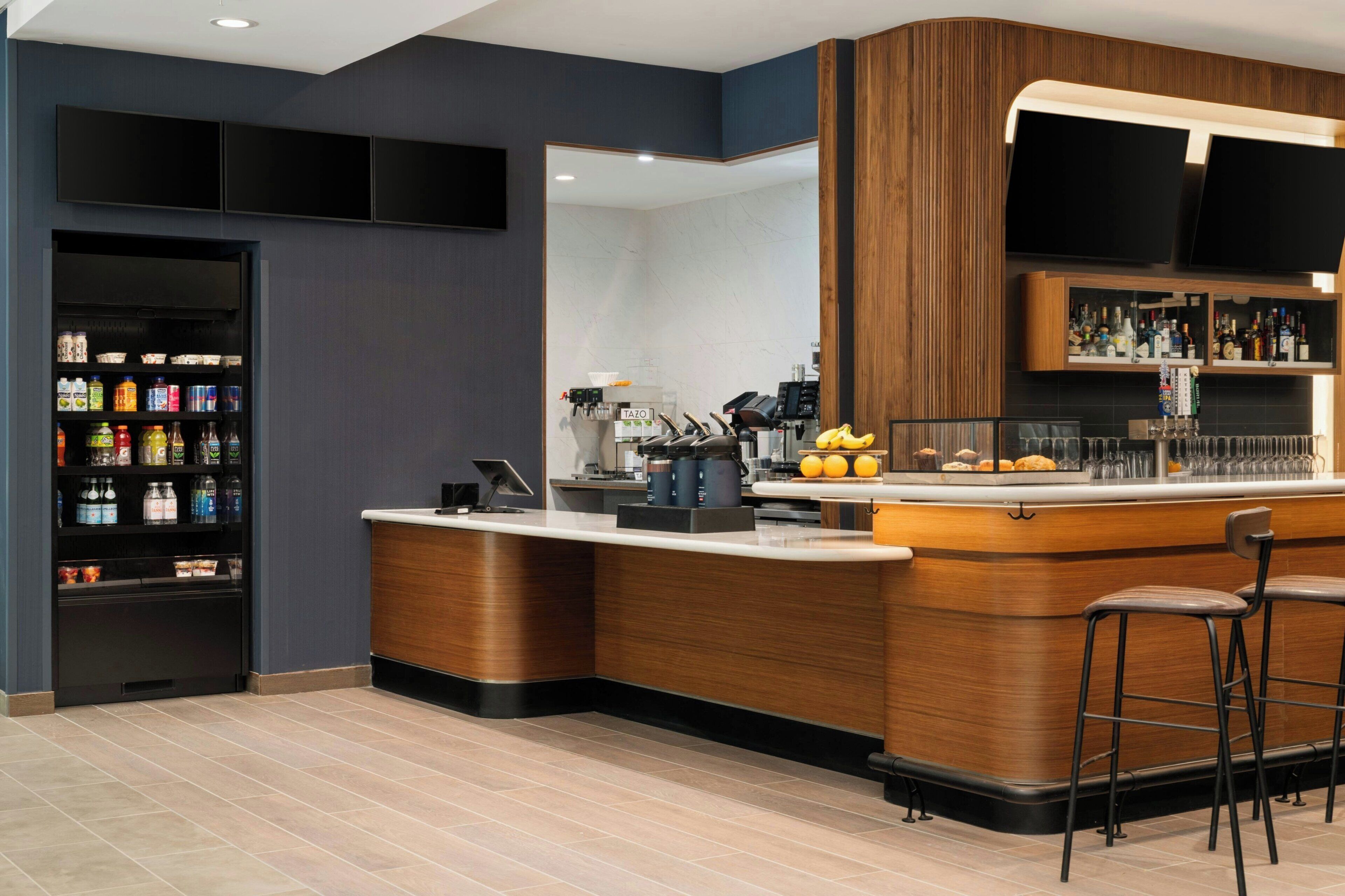 A modern bar area with a counter, stools, a beverage dispenser, and a selection of drinks.
