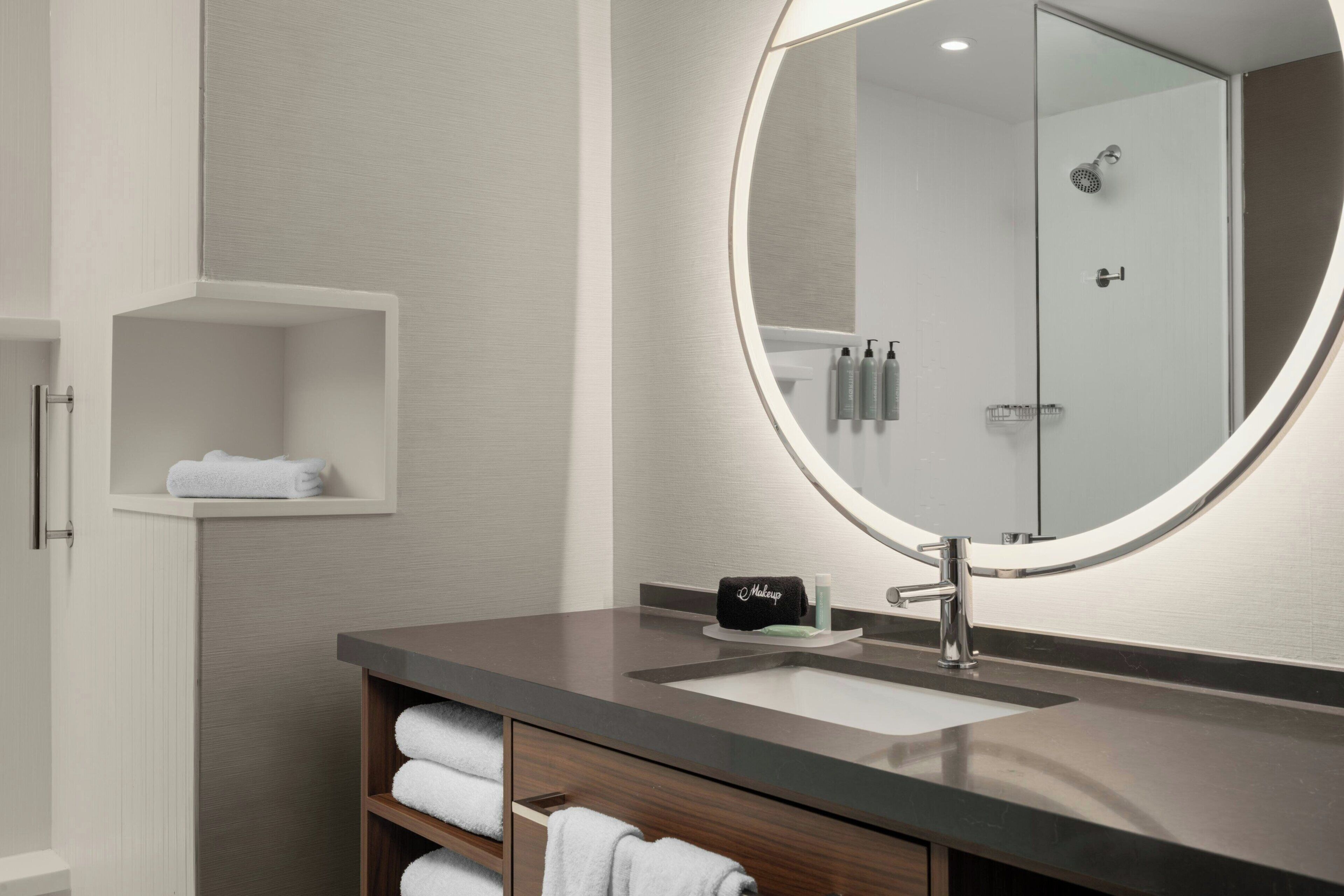 A modern bathroom with a round mirror, a sink, and a shower area.