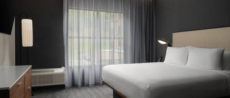 Ein Hotelzimmer mit Bett, Schreibtisch, Stuhl, Lampe und einem fensterbepflanzten Fenster.