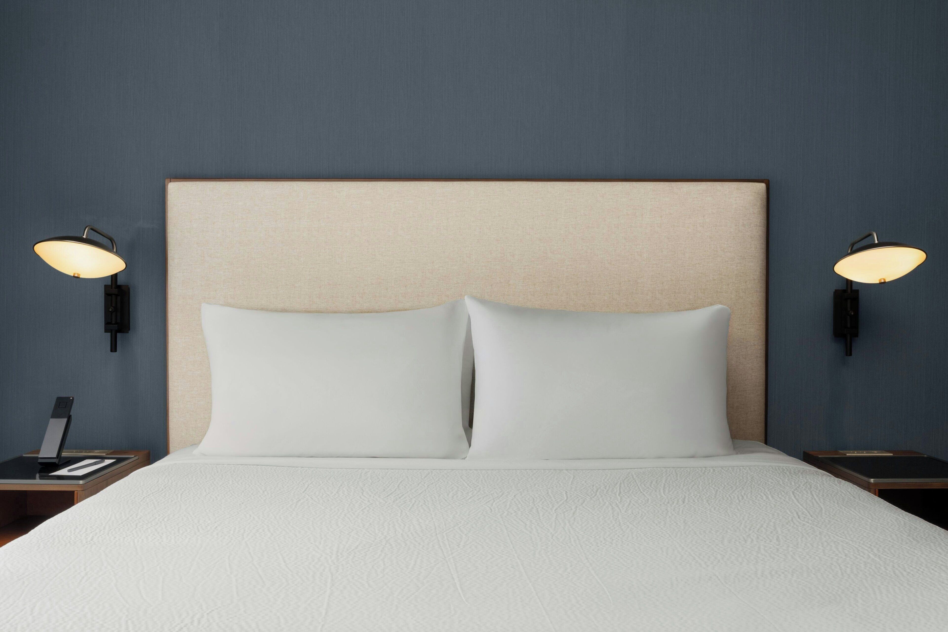 A hotel room with a bed, two bedside tables, and wall-mounted lamps.