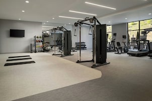 Un gimnasio moderno con varios equipos de ejercicio, un televisor montado en la pared y un amplio ventanal que proporciona luz natural.