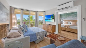 Ein modernes Schlafzimmer mit einem großen Bett, einem Fernseher und einem Balkon mit Blick auf Palmen.