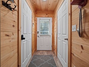 Un pasillo con paredes de madera, una puerta blanca y un ventanal con persianas.
