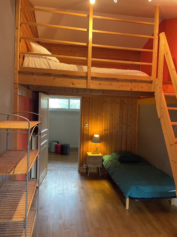 Une chambre avec un lit superposé, une échelle en bois, une petite table de chevet avec une lampe et un lit simple.