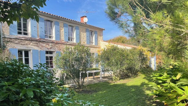 A stone building with blue shutters, a garden with various plants, and a clear sky.