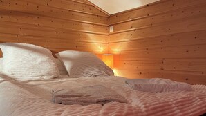 A cozy room with a wooden sloped ceiling, a bed with white bedding, and a wall-mounted light fixture.