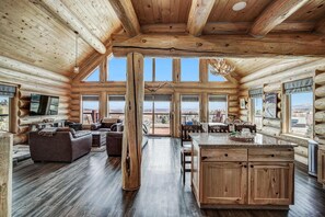 Interior espacioso de una cabaña de troncos, con una amplia sala de estar, cocina con armarios de madera y grandes ventanales que ofrecen vistas al exterior.