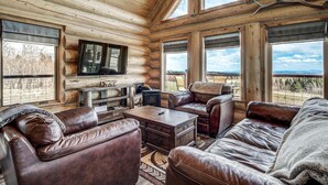 A log cabin interior with leather furniture, a flat-screen TV, and large windows offering a scenic view. - Thick Spike Lodge - Huge space for the whole group! (Fairplay)