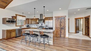 A modern kitchen with wooden cabinets, stainless steel appliances, a central island with bar stools, and pendant lighting. - Platte River Valley Cabin (Fairplay)