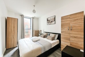 Un dormitorio moderno con una cama, un armario de madera, una mesita de noche, una lámpara y un cuadro en la pared.