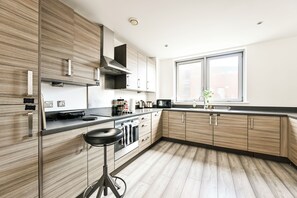 A modern kitchen with wooden cabinetry, a black countertop, and a window providing natural light. - Spacious 3-bed Apartment in Stratford | Free Parking & Terrace (Greater London)