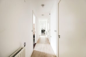 Un couloir aux murs blancs, avec un radiateur et une porte au fond.
