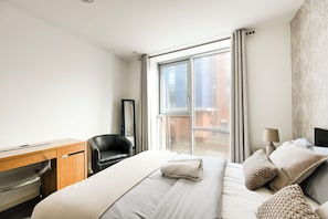 Une chambre d’hôtel comprenant un lit, un bureau, une chaise, une fenêtre avec des rideaux et une vue sur l’extérieur.