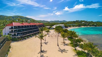 Een hotel aan het strand met meerdere balkons, een zandstrand en een helder uitzicht op de turquoise zee.