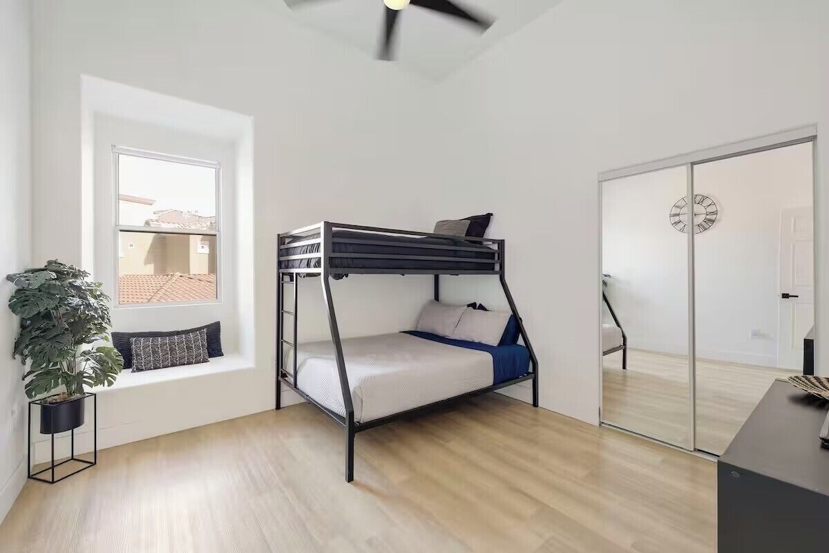 Een kamer met een stapelbed, een raam met uitzicht, een potplant en een deur met een klok.