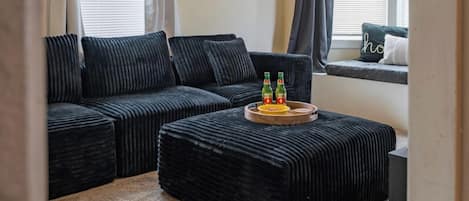 Una sala de estar con un sofá modular, un reposapiés a juego y un asiento junto a la ventana con cojines.