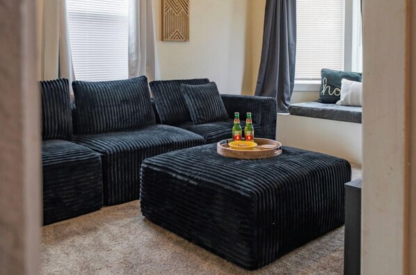 A living room with a sectional sofa, a matching ottoman, and a window seat with cushions.