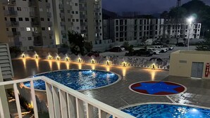 Uma área de piscina no terraço com várias piscinas, um deck de madeira e um guarda-corpo branco.