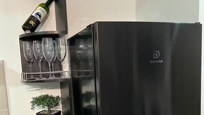 Geladeira preta com dispensador de água e uma garrafa de vinho em uma prateleira.