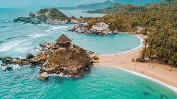Paisagem costeira com praia, águas turquesa cristalinas e afloramentos rochosos.