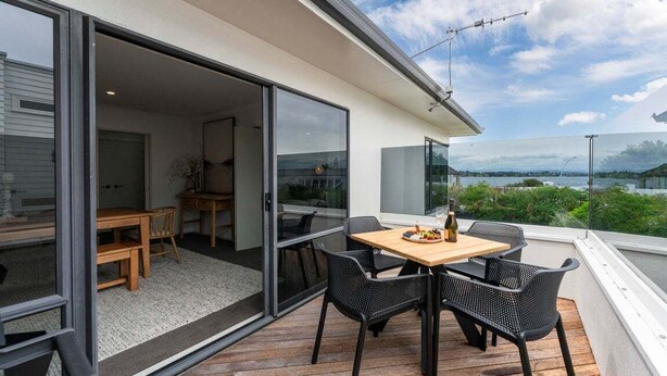 Uma área de refeições ao ar livre com mesa e cadeiras, vista da paisagem e porta de vidro deslizante que dá para um espaço interno.