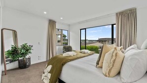 Quarto de hotel moderno com uma cama grande, uma planta em vaso e vista para o exterior.