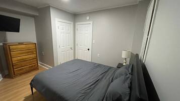 Un dormitorio con cama, cómoda, mesita de noche con lámpara y dos puertas.