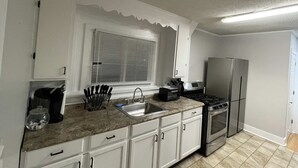 A kitchen with white cabinets, a granite countertop, a stainless steel refrigerator, a stove, and a window with blinds.