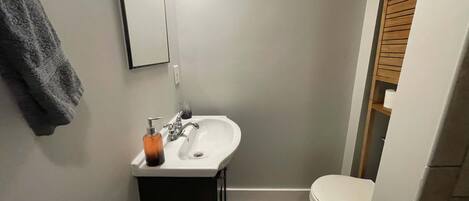 A bathroom with a white sink, a mirror, a towel hanging on the wall, and a toilet.