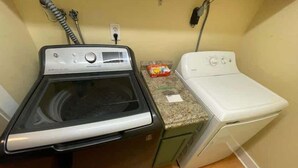 A compact laundry area with a front-loading washer and dryer, a small countertop, and a vacuum cleaner.