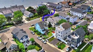 An aerial view of a residential area with houses, a road, and a body of water in the background.