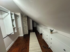 A narrow hallway with wooden flooring, white storage units, a brick accent wall, and a white dresser with a plant. - 3-bedroom house in a peaceful Saint Paul neighborhood with a fenced in back yard (Saint Paul)