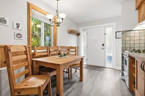 A dining area with a wooden table and chairs, a chandelier, and a view of the outdoors through a glass door. - Forest & Sea Views - Jetted Tub - Walk to Beaches & Wild Pacific Trail (Ucluelet)