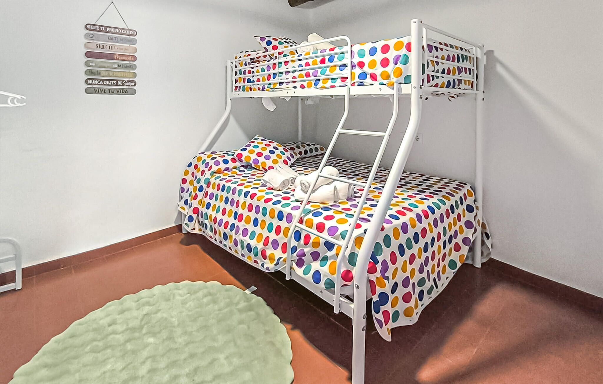 Un lit superposé avec une couvre-lit à pois, un tapis vert et des affiches motivantes au mur.