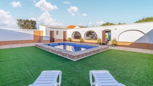 Zona piscina con due lettini, una piccola vasca e un edificio bianco con porte ad arco.