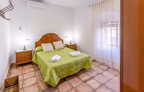 Une chambre à coucher avec un lit en bois, une literie verte, une table de chevet, une lampe de chevet et une fenêtre ornée de rideaux légers.