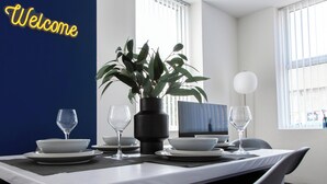 Una mesa de comedor dispuesta con platos, tazones y copas de vino, una planta en maceta y un cartel que dice 'Welcome' en la pared.