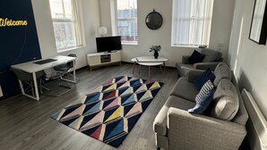 A modern living room with a sofa, a coffee table, a TV, and a patterned rug. - Residency apartments liverpool (Bootle)