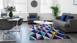 A modern living room with a dining area, grey sofas, a colorful rug, and a potted plant. - Residency apartments liverpool (Bootle)