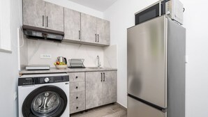 Een kleine keuken met een wasmachine, een koelkast en grijze kastjes.