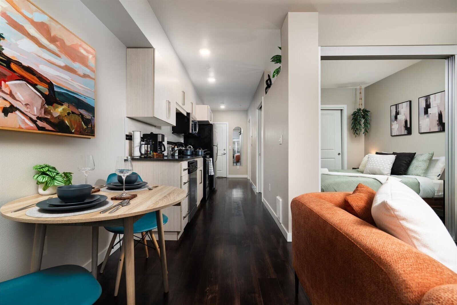 A modern kitchen with dark wood flooring, white cabinets, and a dining area with a table and chairs.